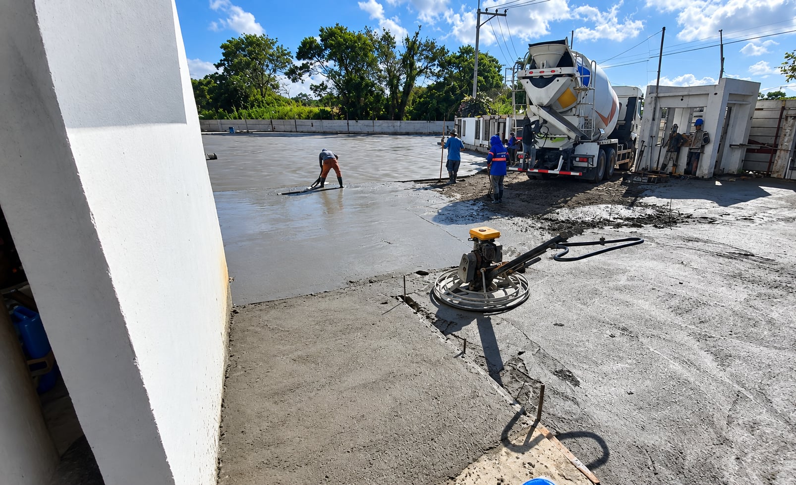 Crew power-troweling a fresh concrete slab next to a mixer truck